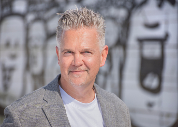 Dr. Stephan Weichert im grauen Sakko vor einer Wand mit grauen Graffiti